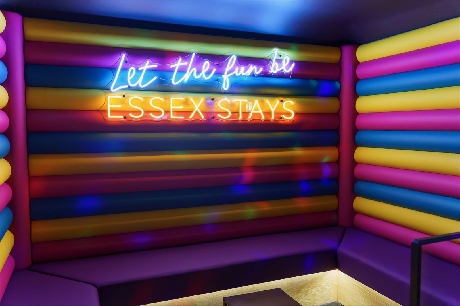 Karaoke room with padded rainbow walls and a neon sign reading Let the fun be Essex Stays